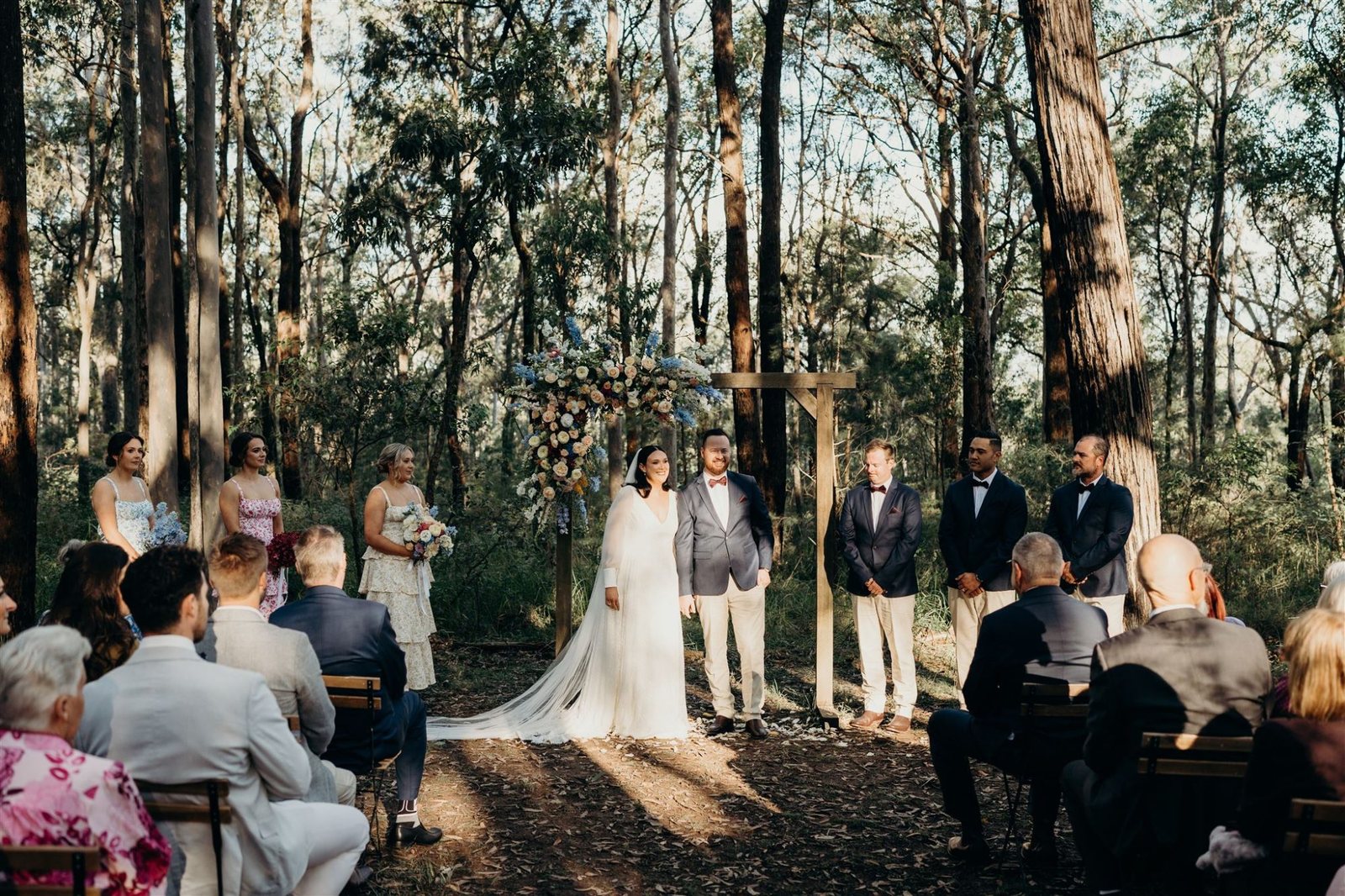 A ceremony at the timber arbour in the gum forest, guests on crossback chairs